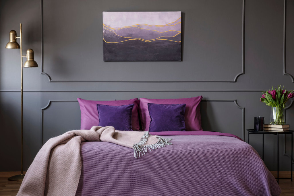 Pink blanket on violet bed in elegant bedroom interior with painting on grey wall with molding