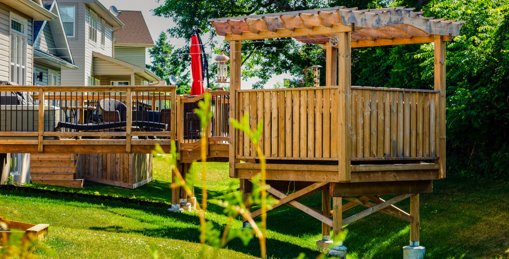 Raised backyard wooden deck and gazebo in a treed backyard, behind a row of houses